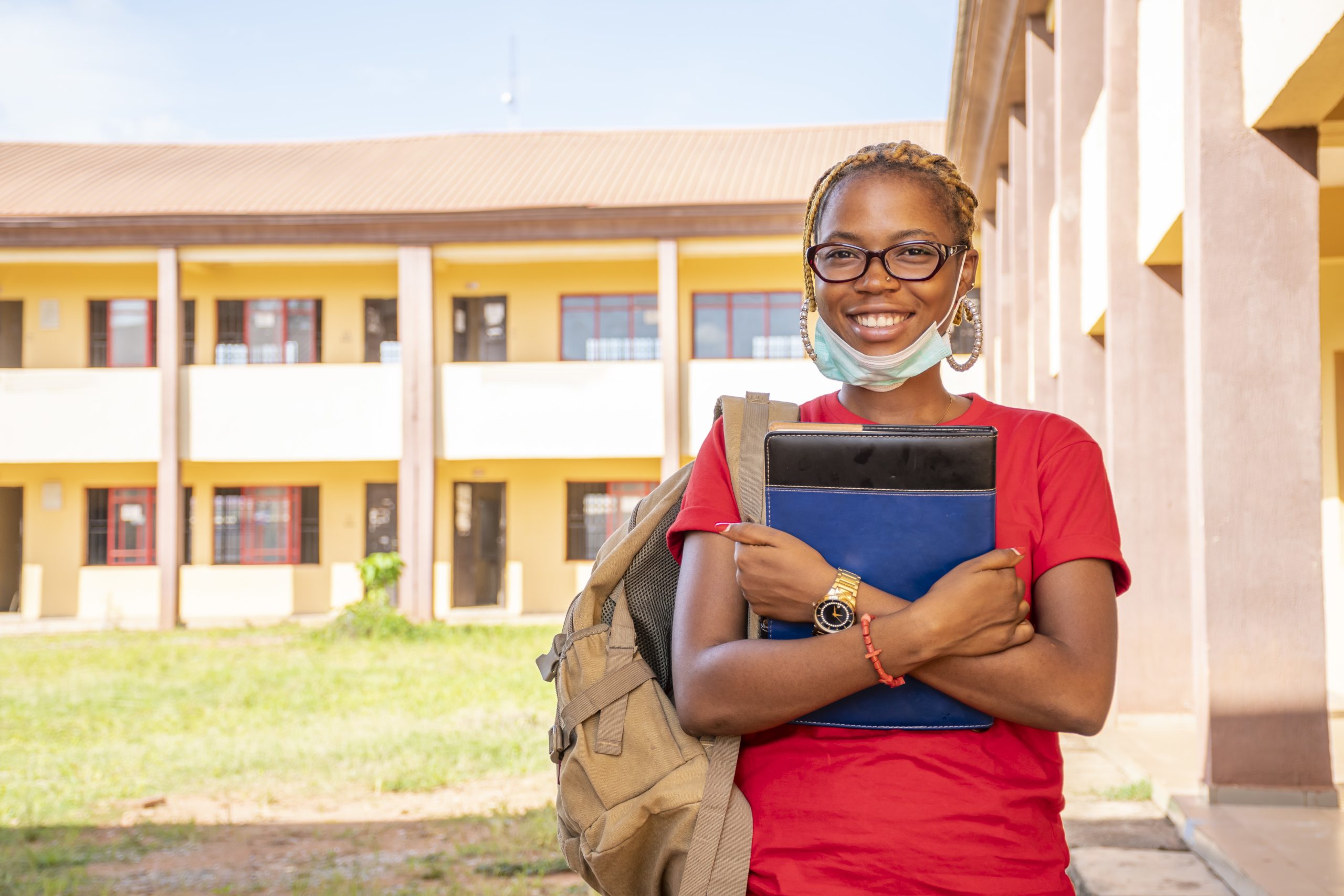 Young African female student with a facemask holding her textbooks at a campus area